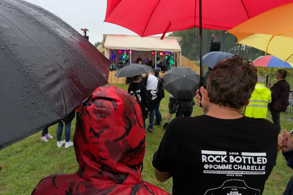 Festivalgangers onder paraplu’s, een van hen in een Rock Bottled T-shirt